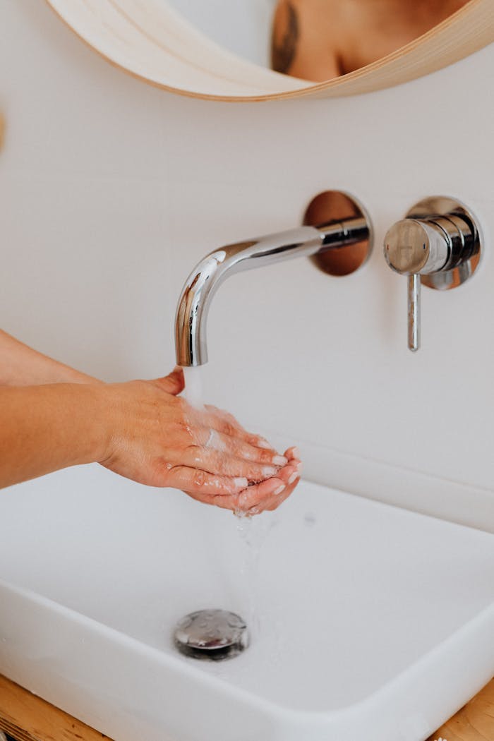 A close-up of hands being washed in a modern bathroom with a stainless steel faucet.